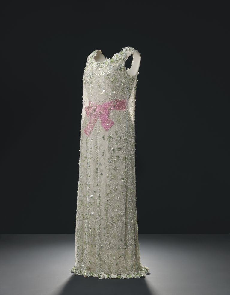 Đầm dạ hội bằng lụa màu kem phủ ngoài một lớp vải tulle trong suốt thêu và đính đá màu xanh nhạt, thắt nơ hồng ngang eo, thiết kế năm 1966