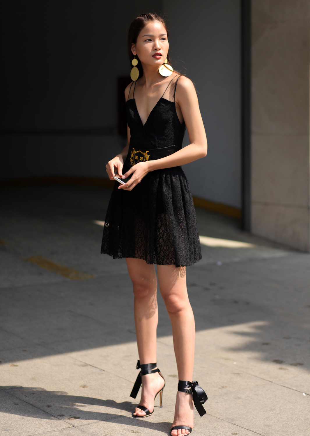 Người mẫu Chà Mi sử dụng phụ kiện là đôi khuyên ánh vàng; cùng thắt lưng với hoạ tiết cam tô điểm cho bộ váy đen.
