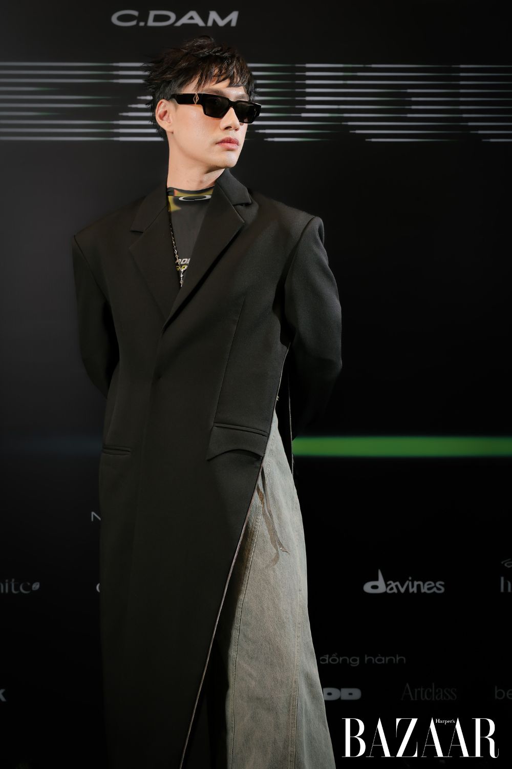 Diện trang phục C.Dam, NTK Lý Quí Khánh phối “racer jumpsuit” cùng thiết kế áo blazer dáng dài có kết cấu mở khoá chéo từ sườn ra phía trước.